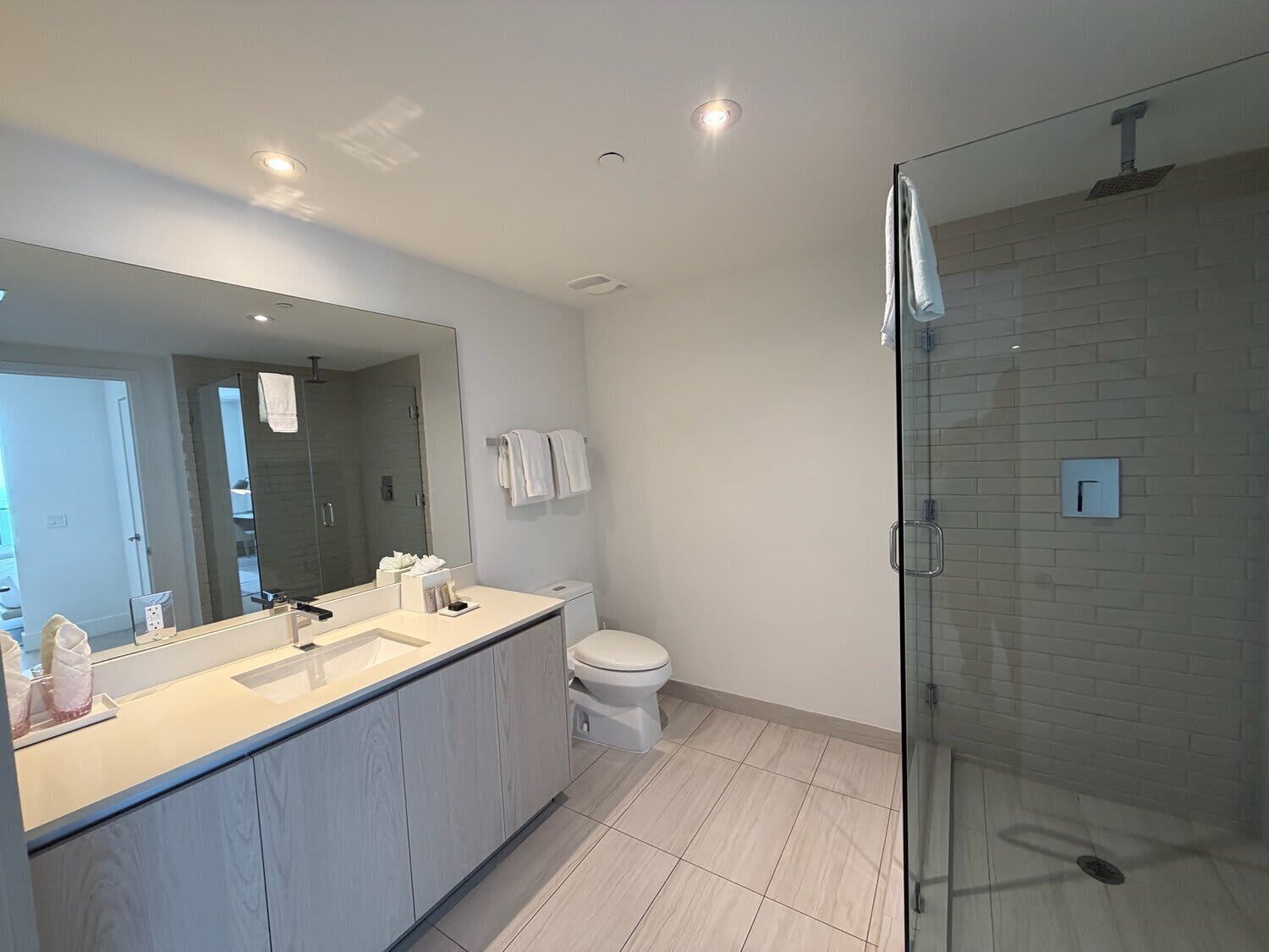 A modern bathroom with a large mirror, a glass shower enclosure, and a toilet.