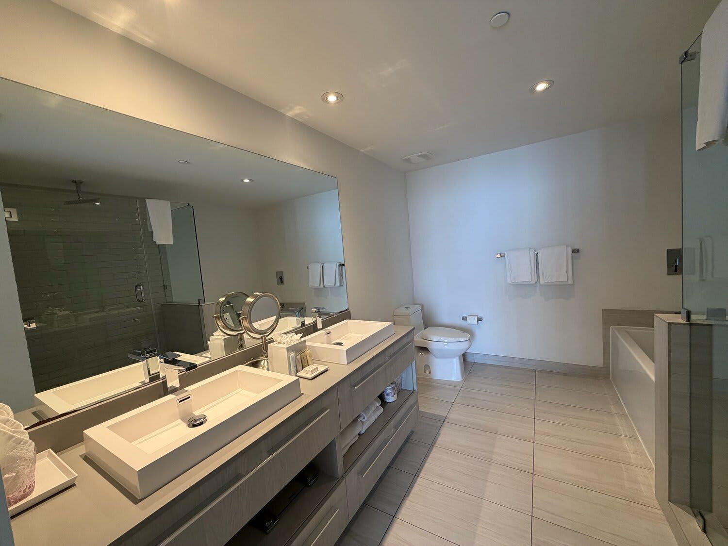 Ein modernes Badezimmer mit einem großen Spiegel, zwei Waschbecken, einer Toilette und einer Duschkabine.