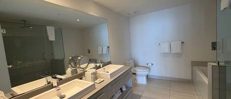 Ein modernes Badezimmer mit einem großen Spiegel, zwei Waschbecken, einer Toilette und einer Duschkabine.
