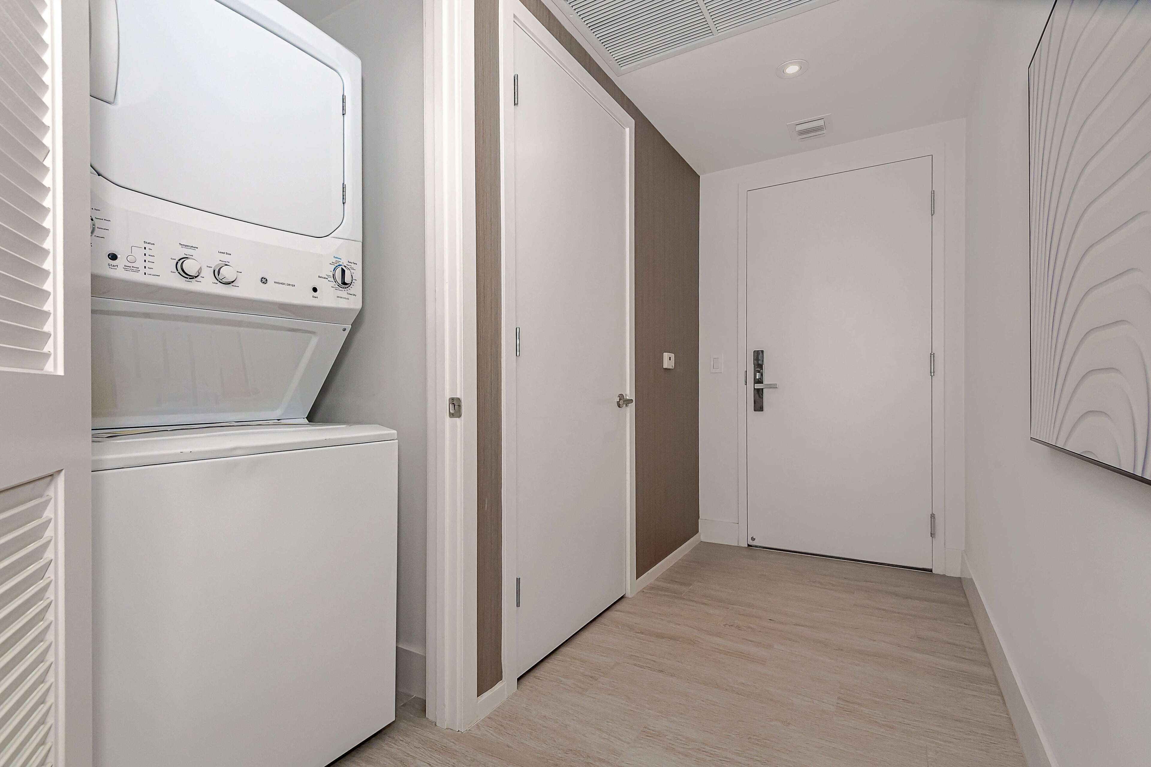 Un couloir avec un lave-linge blanc, une porte et un mur orné d’un motif en relief.