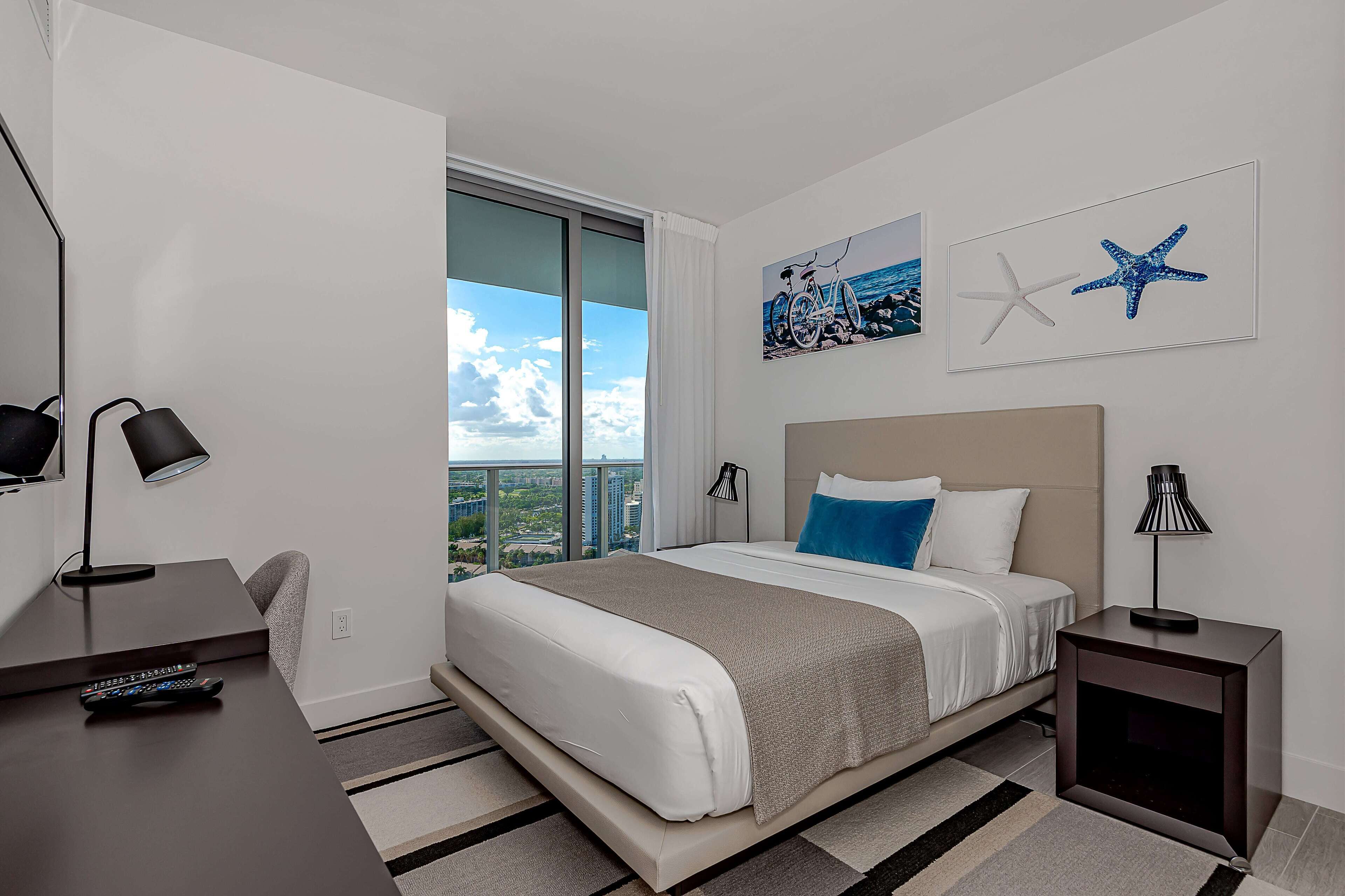 A modern hotel room with a large bed, a desk, and a view of the city.