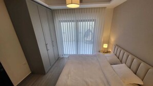 Una habitación de hotel moderna con una cama grande, un armario y una ventana con cortinas de gasa.