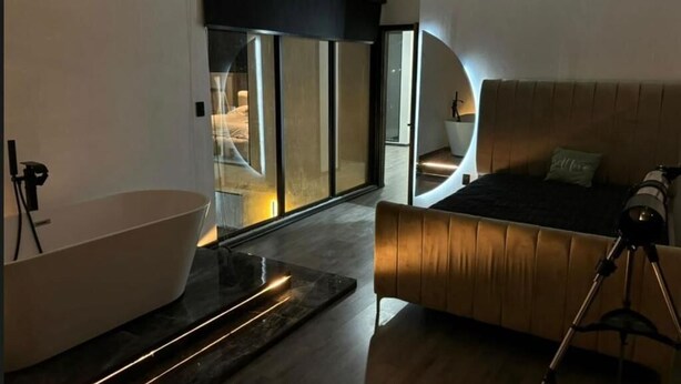 Un dormitorio moderno con una bañera grande, una cama con cabecera de madera y una lámpara de trípode.
