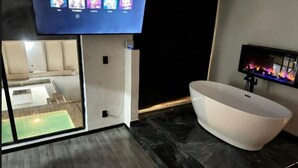 Un baño moderno con una bañera independiente, un espejo grande y un televisor sobre la bañera.