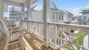 A wooden deck with white railings, overlooking a residential area with white houses and a clear sky.