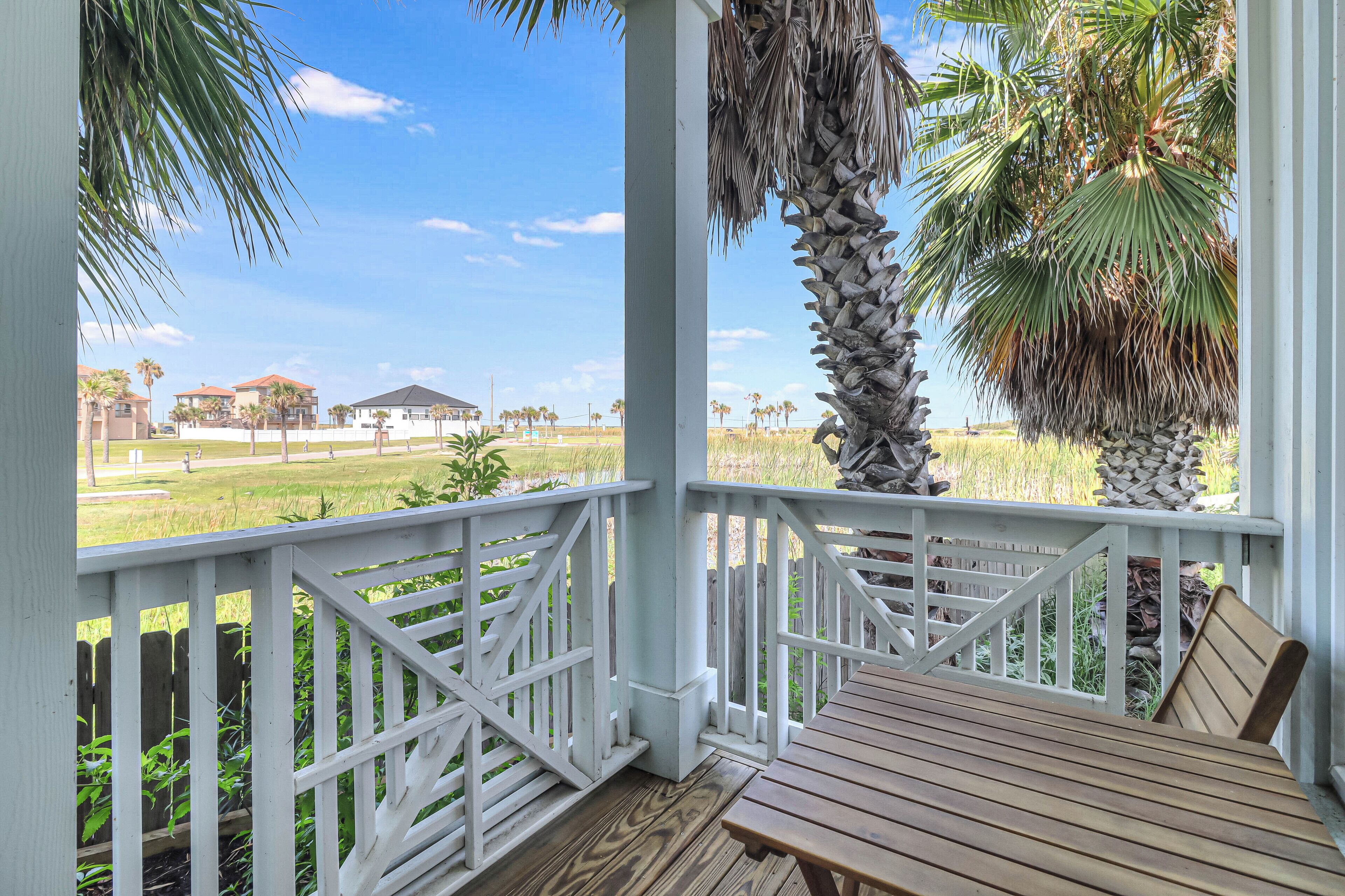 A wooden deck with a white railing, palm trees, and a view of houses in the background.