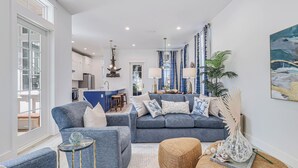A modern living room with a grey sofa, a coffee table, and a side table. There is a kitchen in the background with a dining area.