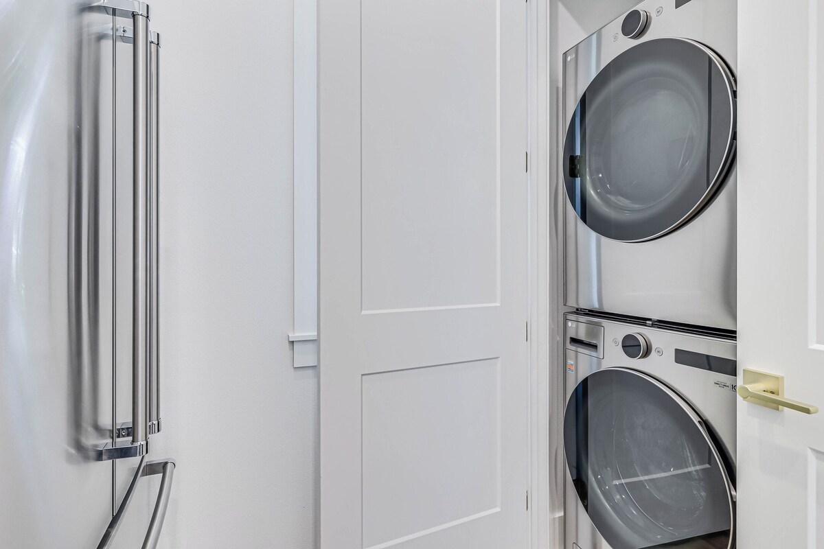 A laundry room with two stacked washing machines, a metal drying rack, and a door with a handle.