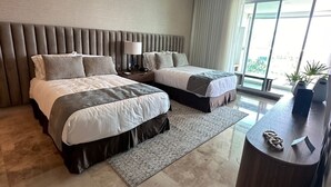 A modern bedroom with two beds, a ceiling fan, a large window, and a wooden side table.