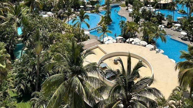 A resort with multiple swimming pools surrounded by palm trees and a mountainous backdrop.