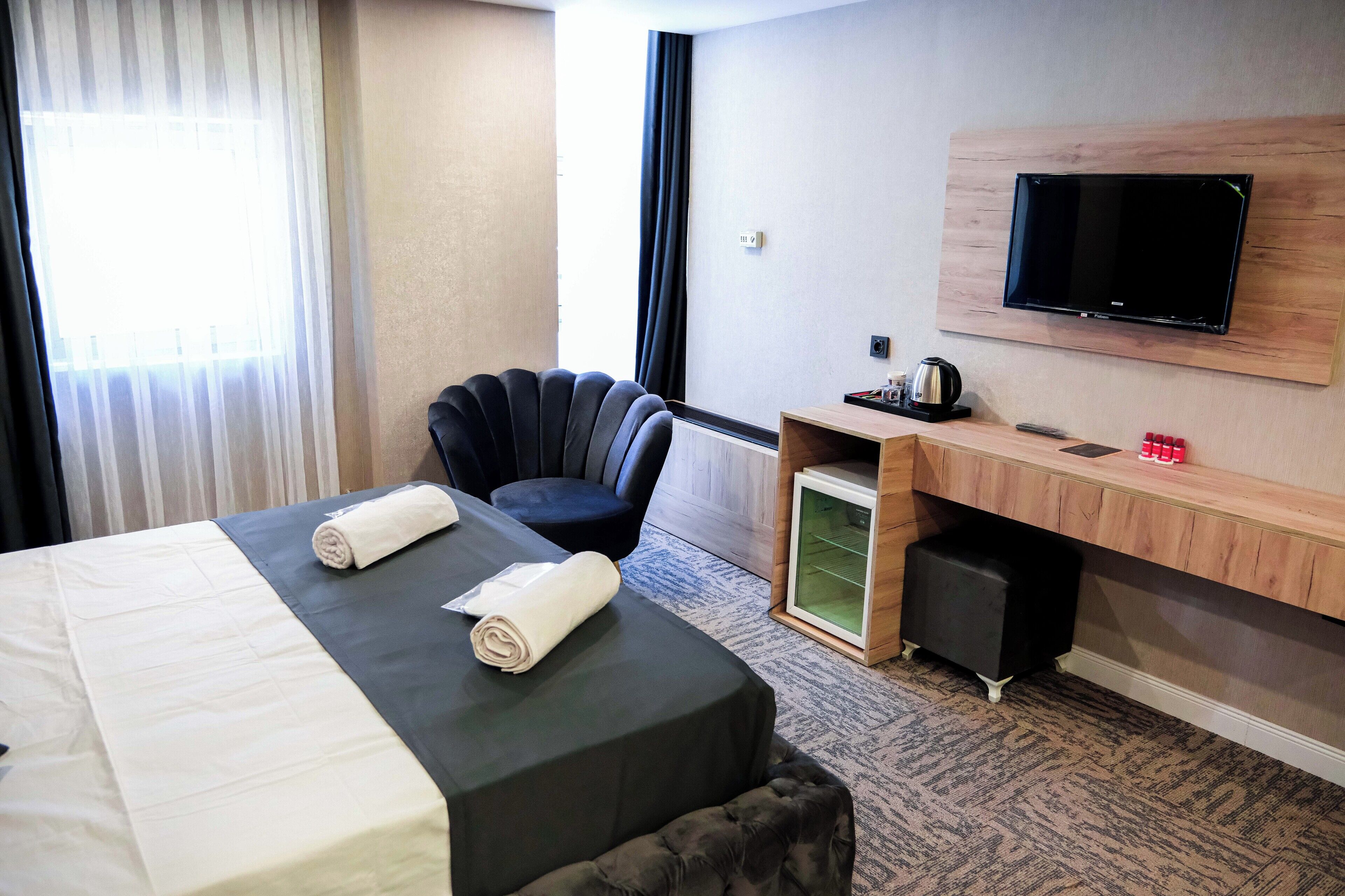 A hotel room with a bed, a desk, a chair, a television, and a window with curtains.