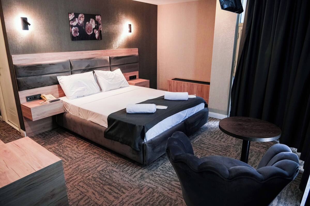 Una habitación de hotel con cama, mesitas de noche, una silla y una pequeña mesa.