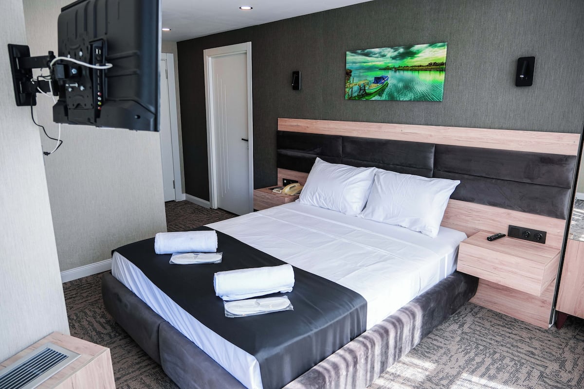 Habitación de hotel con una cama grande, un televisor de pantalla plana montado en la pared, una mesita de noche con lámpara y un cuadro en la pared.