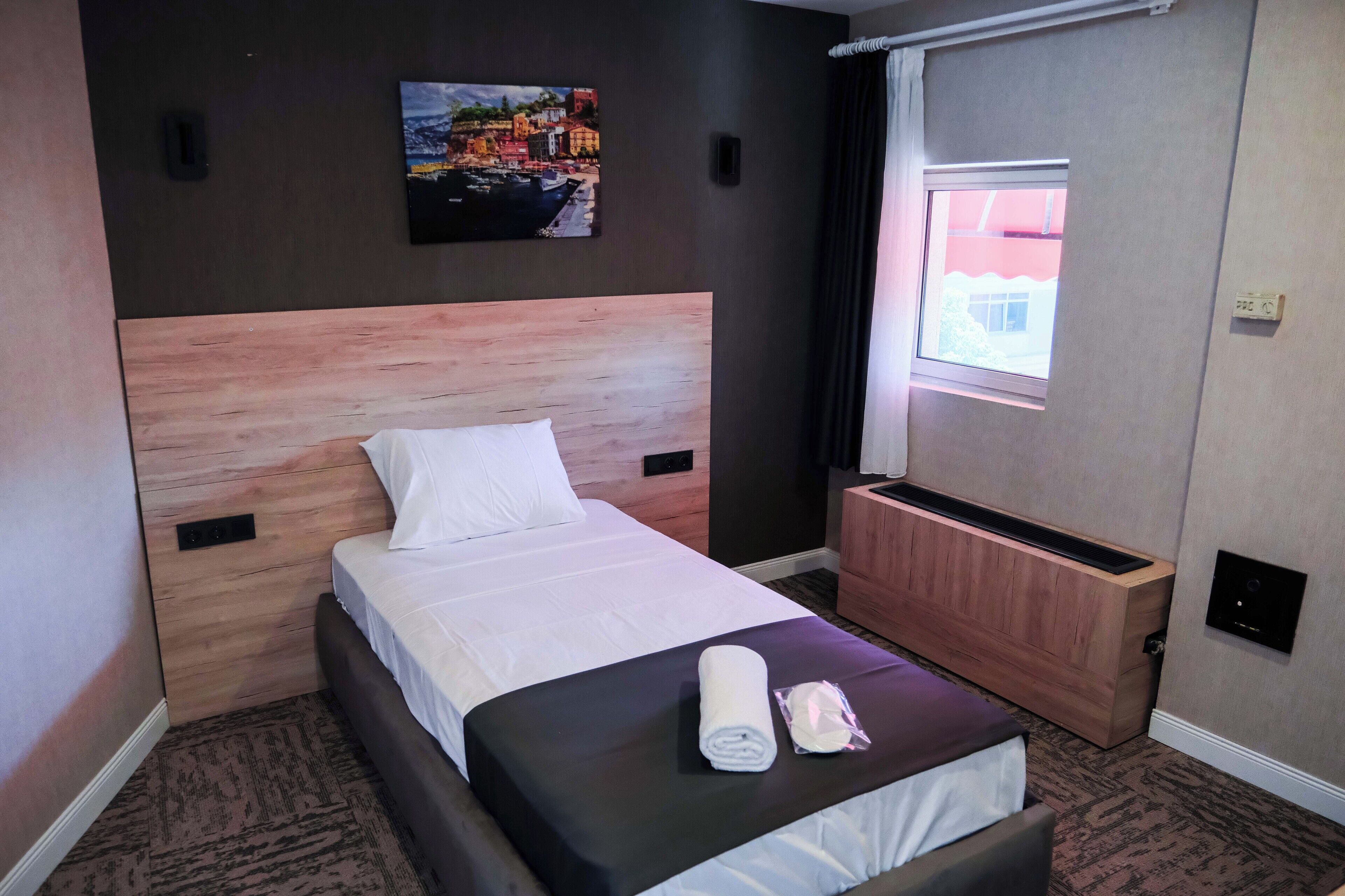 Habitación de hotel con cama, un cuadro colgado en la pared, ventana y calefacción incorporada.