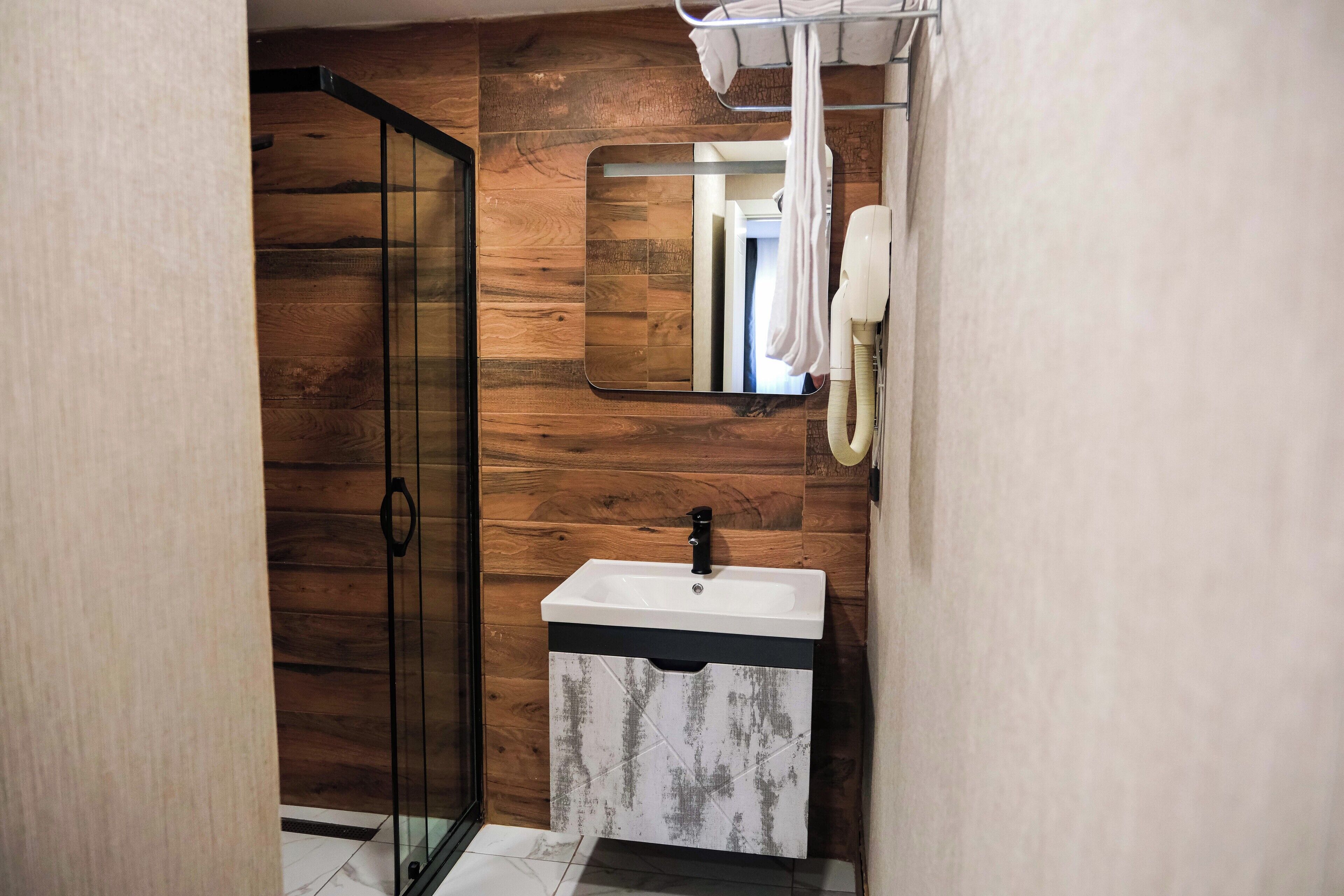 A bathroom with a wooden wall, a glass shower door, a white sink with a black faucet, and a towel hanging on a rack.