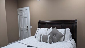 Ein ordentlich bezogenes Bett mit weißer Bettwäsche und grauen Kissen, ein dunkles Holz-Kopfteil und eine weiße Tür mit Griff.