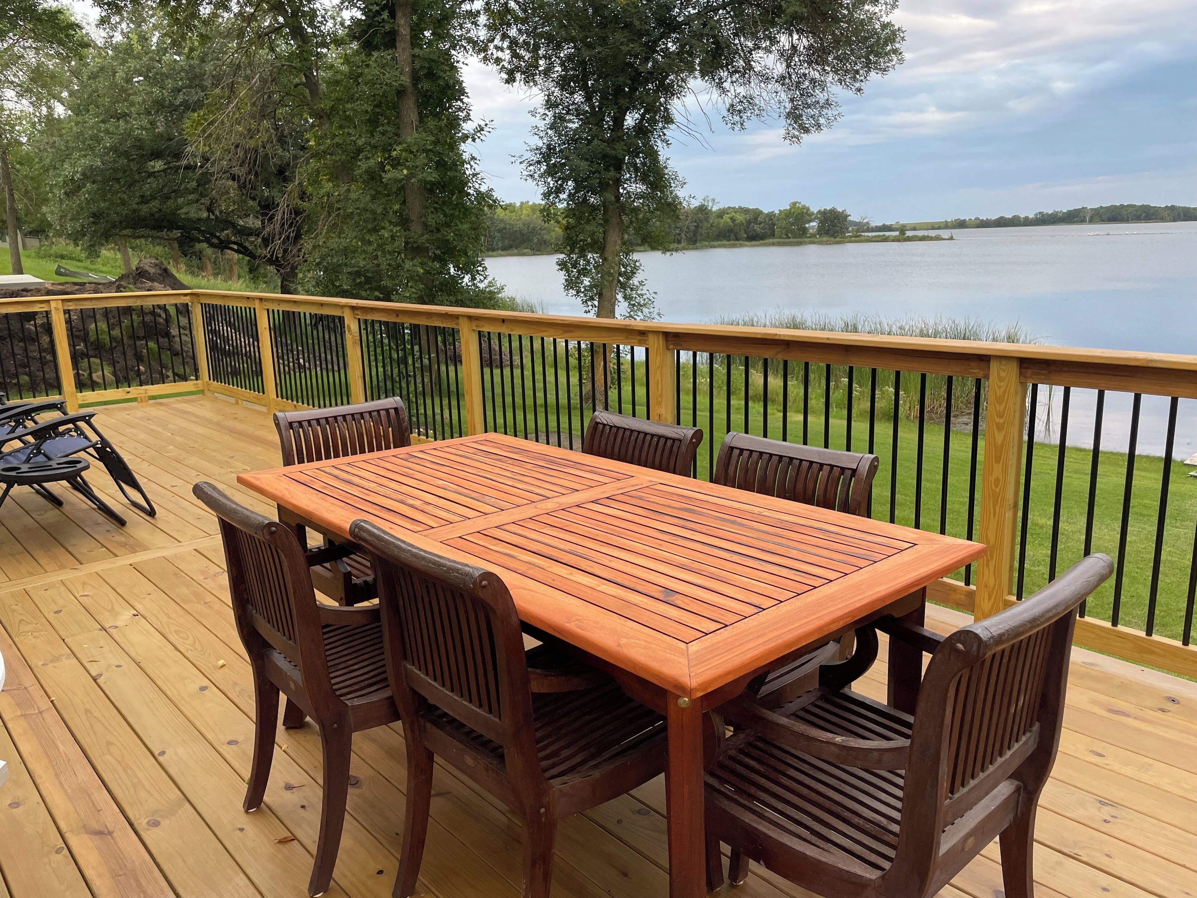 A wooden deck with a table and chairs, overlooking a lake.