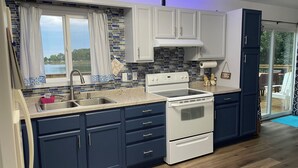 Una cocina moderna con armarios azul oscuro, una estufa blanca y un amplio ventanal con vista al agua.