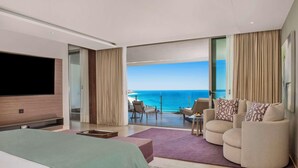 A modern hotel room with a large bed, a TV, a balcony with a view of the sea, and a seating area with a table and chairs. - Grand Velas Los Cabos - All Inclusive (Cabo San Lucas)