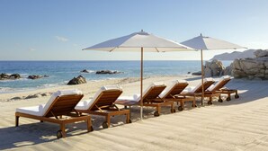 A beach with wooden lounge chairs and white umbrellas. - Grand Velas Los Cabos - All Inclusive (Cabo San Lucas)