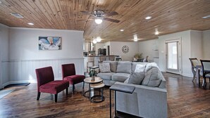 Ein geräumiges Wohnzimmer mit Holzboden, einem grauen Sofa, roten Sesseln und einem Essbereich mit Tisch und Stühlen.
