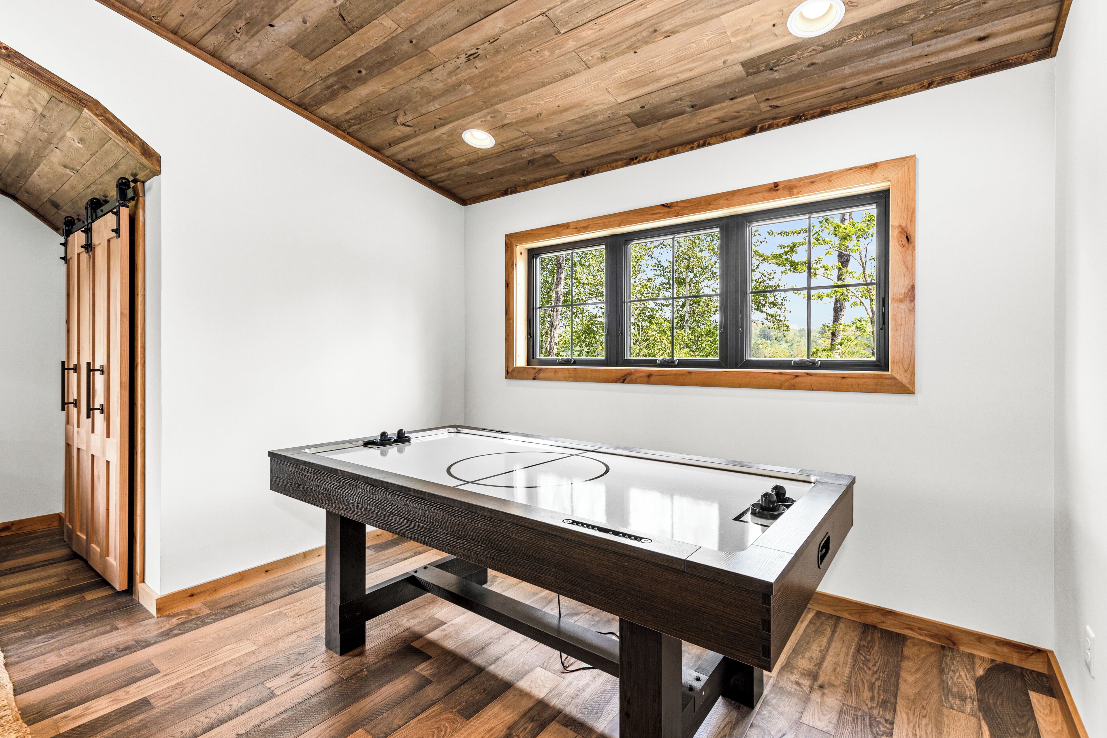 Een kamer met een houten tafel, een raam met uitzicht op bomen en een houten plafond.