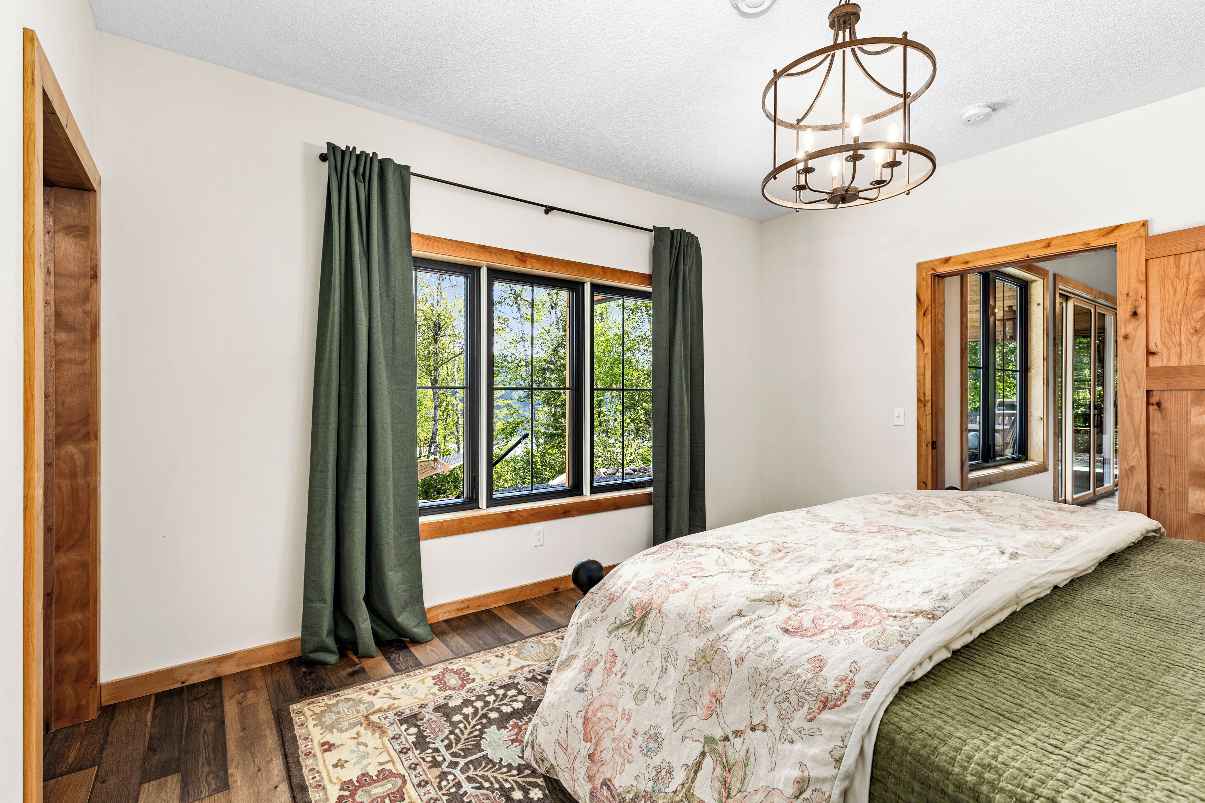 A bedroom with a large window, wooden floor, and a bed with a floral bedspread.
