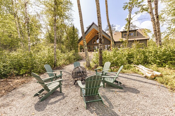 A cabin with a gravel patio, surrounded by trees, and featuring Adirondack chairs and a fire pit. - Aurora Lakeside Retreat (Aurora)