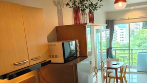 Eine moderne Küche mit integriertem Mikrowellenherd, Kühlschrank und Kaffeemaschine. Ein Essbereich mit Tisch und Stühlen lädt zum Verweilen ein, und ein großes Fenster bietet einen Blick auf die Stadt.