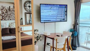Ein modernes Wohnzimmer mit einem Bett, einem an der Wand befestigten Fernseher, einer Essecke mit Tisch und Stühlen sowie einem großen Fenster mit Blick.