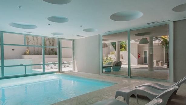 A modern indoor swimming pool with clear glass walls, white lounge chairs, and a minimalist design. - Vizion Carilo by D&G (Carilo)