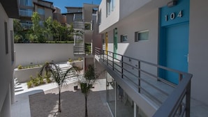 A modern building with a blue door marked "104," a staircase, and a small courtyard with plants. - Vizion Carilo by D&G (Carilo)