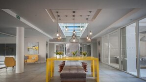 A modern lobby with a central yellow table, a bench, and hanging pendant lights. - Vizion Carilo by D&G (Carilo)