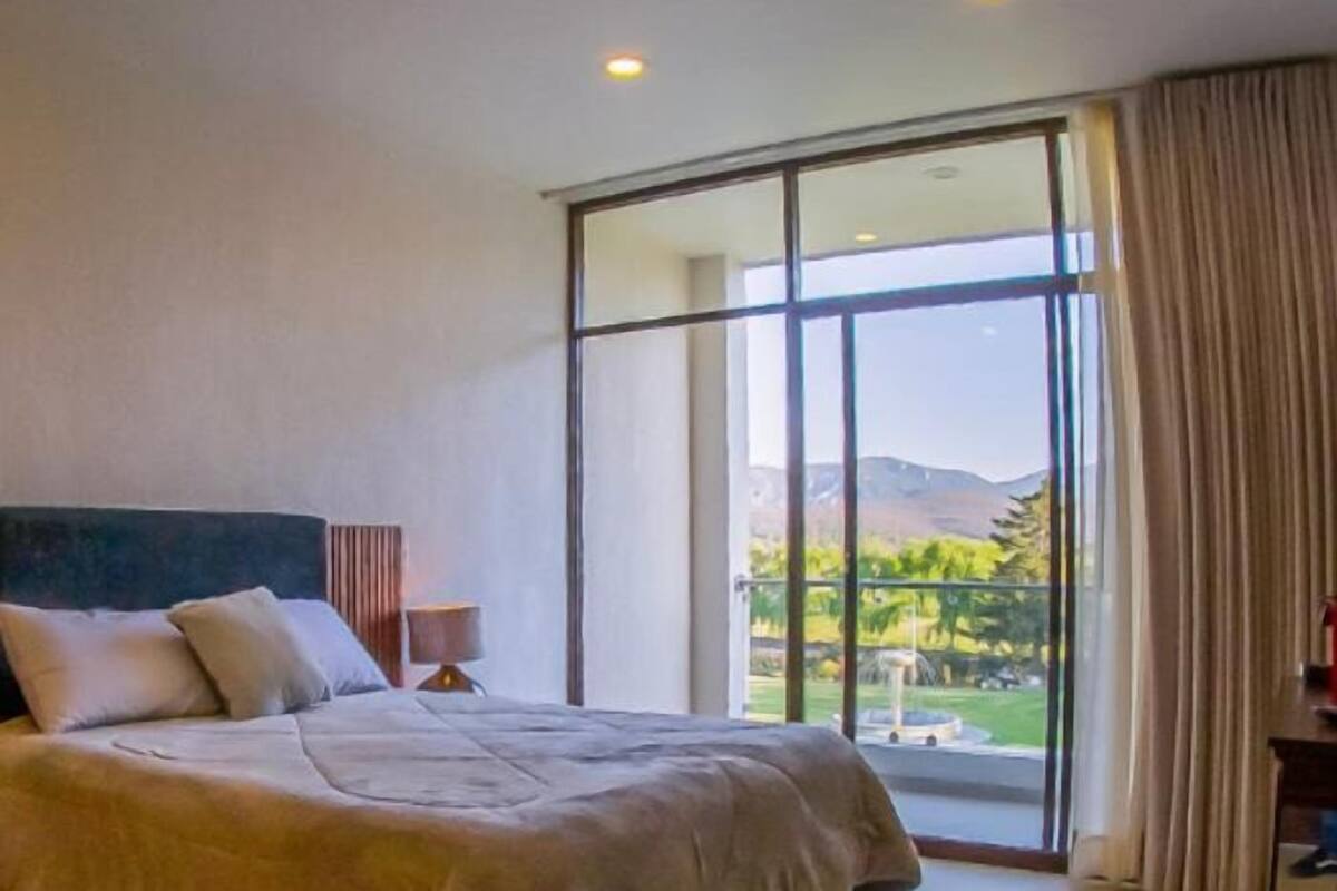 Une chambre d’hôtel moderne dotée d’un grand lit, d’une table de chevet et offrant une vue sur un paysage montagneux grâce à de grandes fenêtres du sol au plafond.