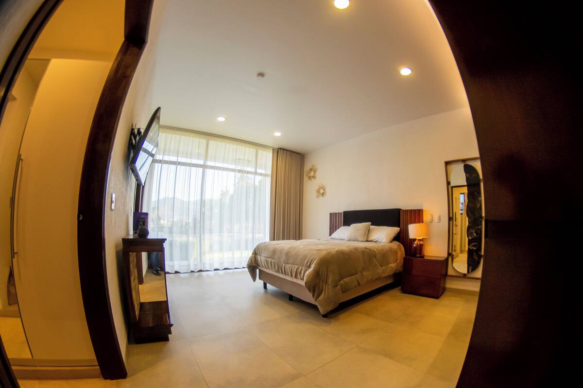Une chambre à coucher avec un lit, une table de chevet, une lampe et une grande fenêtre avec des rideaux.