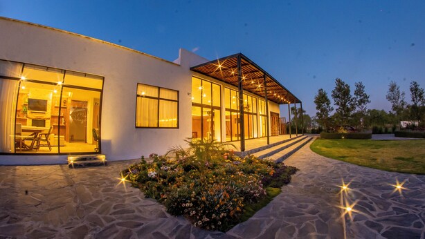 A modern house with large windows, a stone pathway, and a garden with flowers. - Hotel Boutique Monte Penasco (Jilotepec)