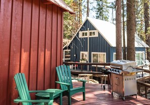 A wooden deck with Adirondack chairs, a grill, and a blue cabin with a white roof.