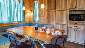 Een houten eetgedeelte met een bank, tafel en stoelen. Er staat een magnetron aan de muur en een waterfles op de tafel.
