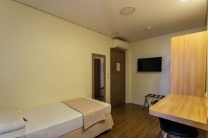 Una stanza piccola e pulita con un letto, una scrivania e una TV montata a parete.