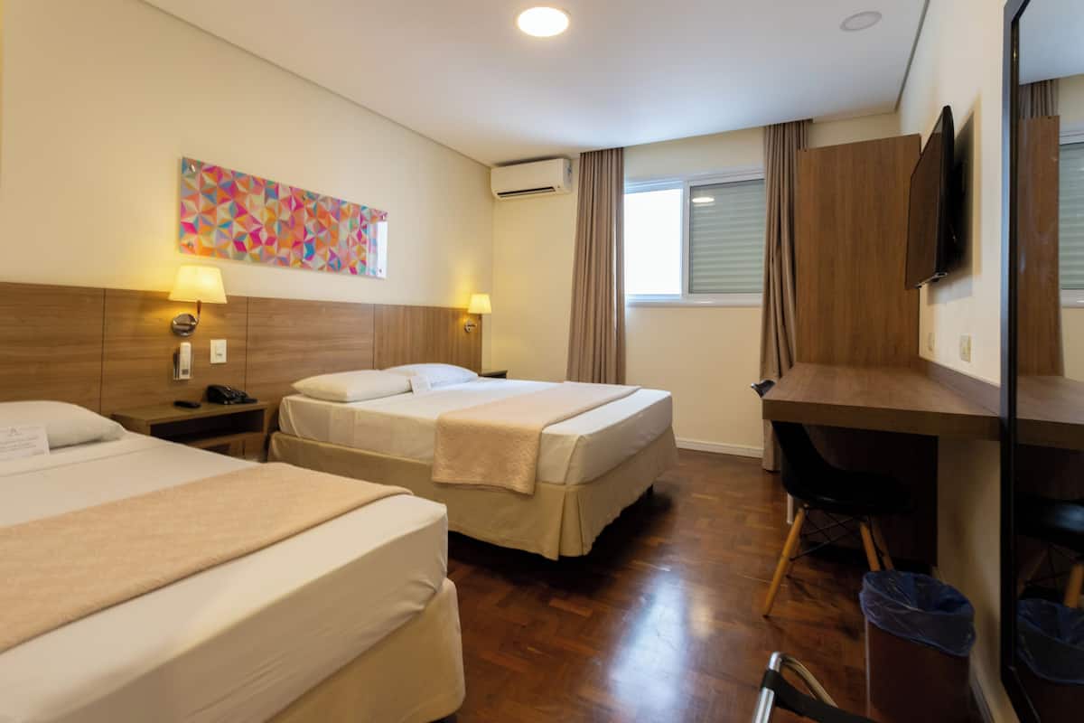 A hotel room with two beds, a desk, a chair, a TV, and a window with curtains.