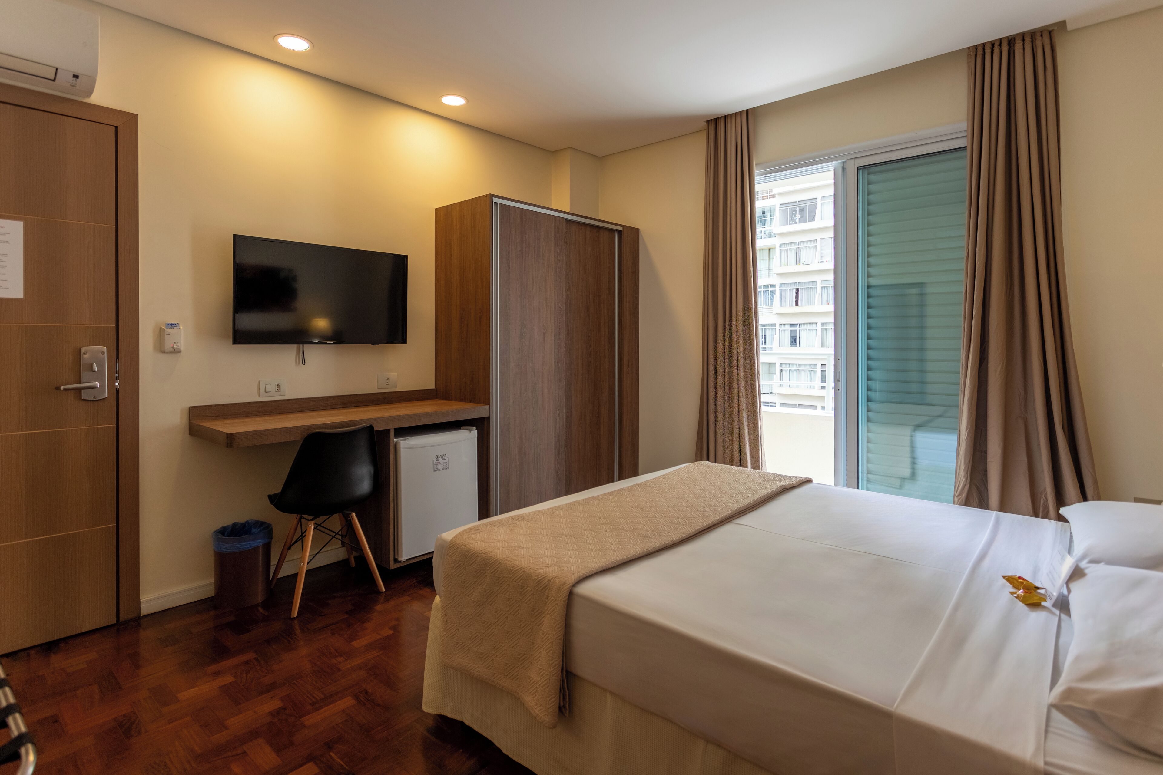 A hotel room with a bed, a desk, a television, a wardrobe, and a window with curtains.