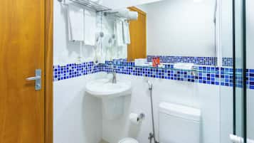 Un baño con lavamanos, inodoro y ducha. Hay toallas y artículos de aseo en la encimera.