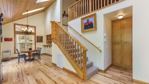 Une pièce spacieuse avec un escalier en bois, un coin repas comprenant une table et des chaises, et une grande porte en bois.
