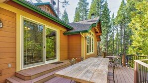 Une terrasse en bois avec une table de pique-nique et des chaises, entourée d’une clôture en bois et d’arbres.