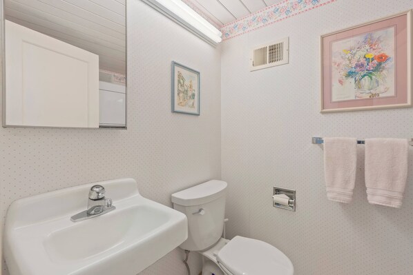 A bathroom with a white sink, toilet, and a framed floral painting on the wall.