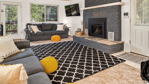 A modern living room with a fireplace, a sofa, and a patterned rug. - Shaver Lake Cabin with Deck and Mountain Views (Auberry)
