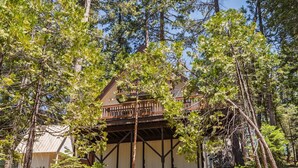 A rustic cabin with a wooden deck and a covered porch, surrounded by trees. - Shaver Lake Cabin with Deck and Mountain Views (Auberry)