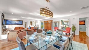 A modern dining area with a glass table, leather chairs, and a hanging light fixture.