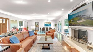 A modern living room with a leather sofa, a coffee table, and a fireplace. There is a dining area in the background with a view of the ocean.