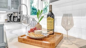 A kitchen counter with a bottle of Caymus Vineyards, a plate of cheese and crackers, and two glasses of wine.
